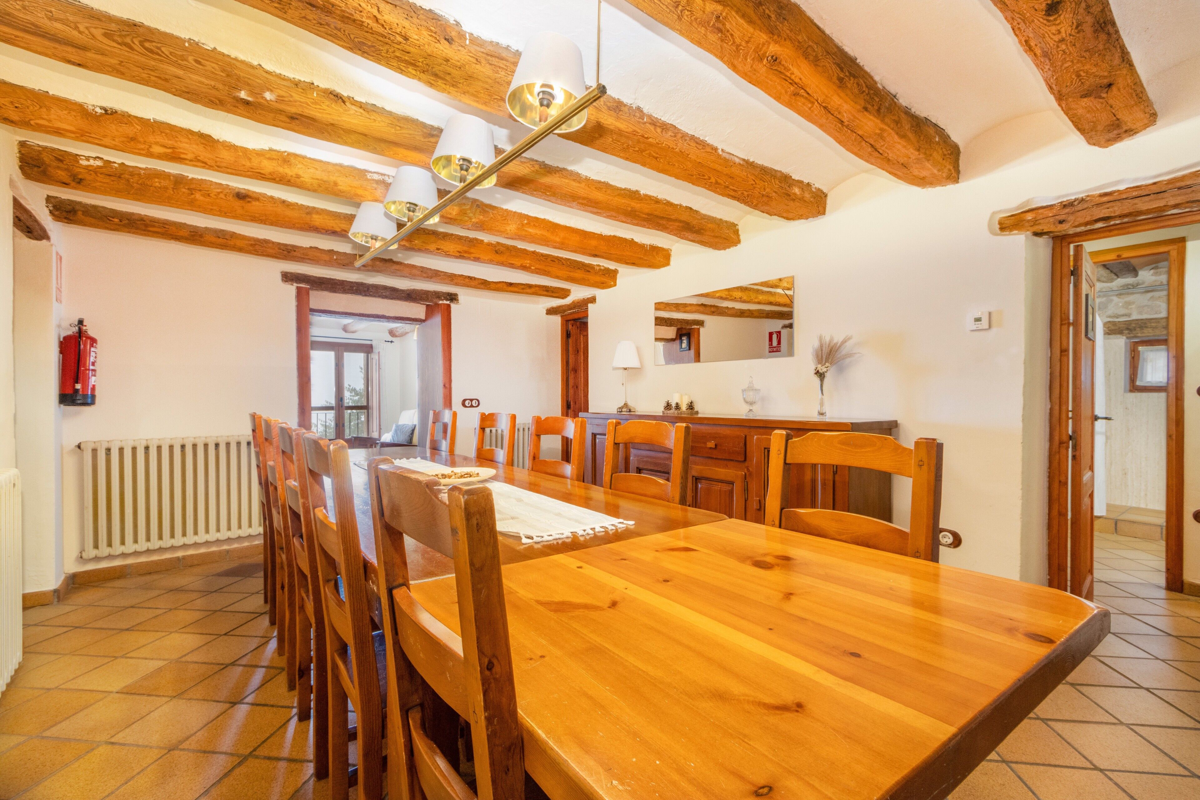 Un comedor con una mesa y sillas de madera, techo con vigas a la vista y un radiador en la pared.