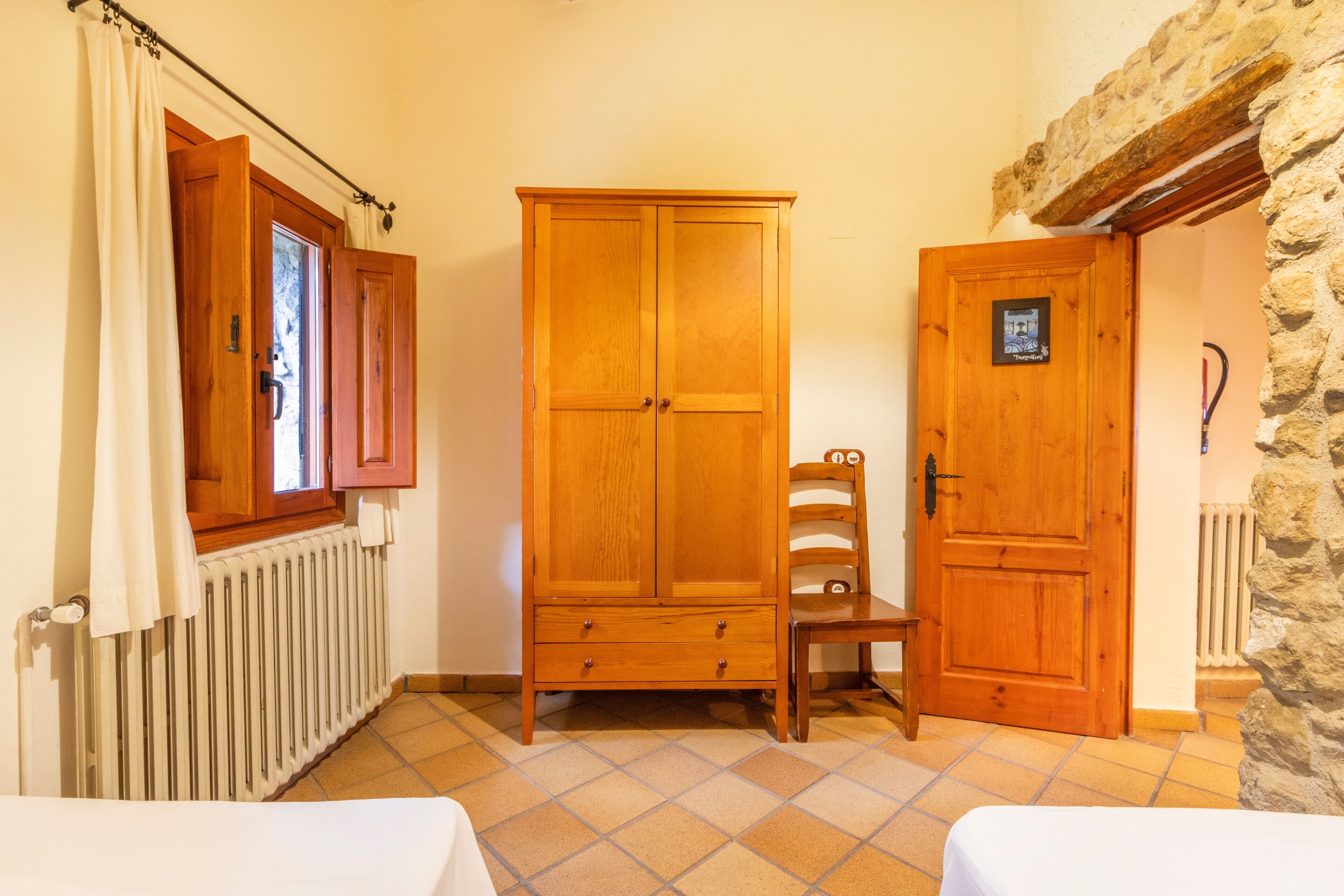 Een kamer met een houten garderobe, een stoel, een radiator en een stenen muur.