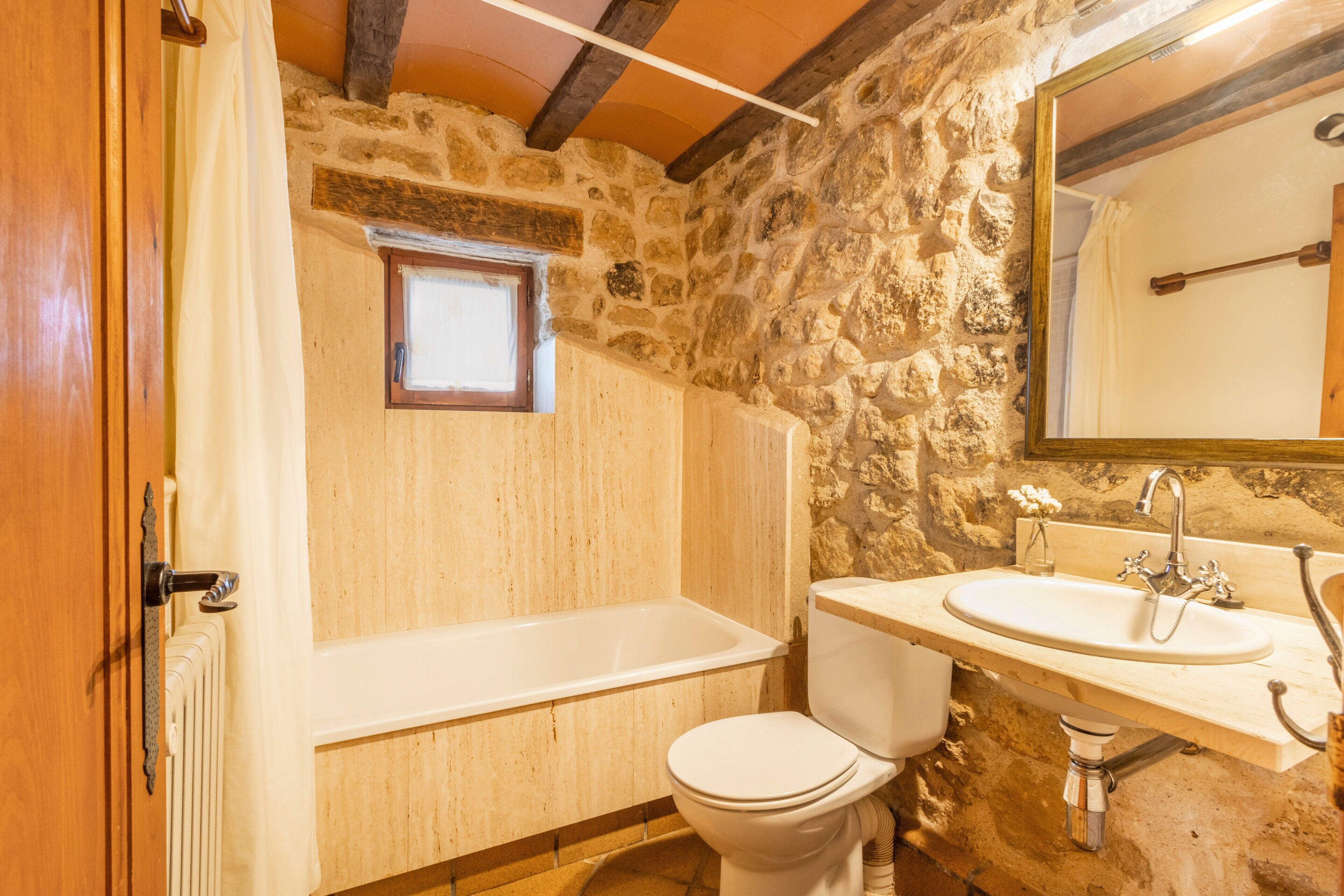 Un bagno con parete in pietra, una vasca, un WC e un lavandino con specchio.