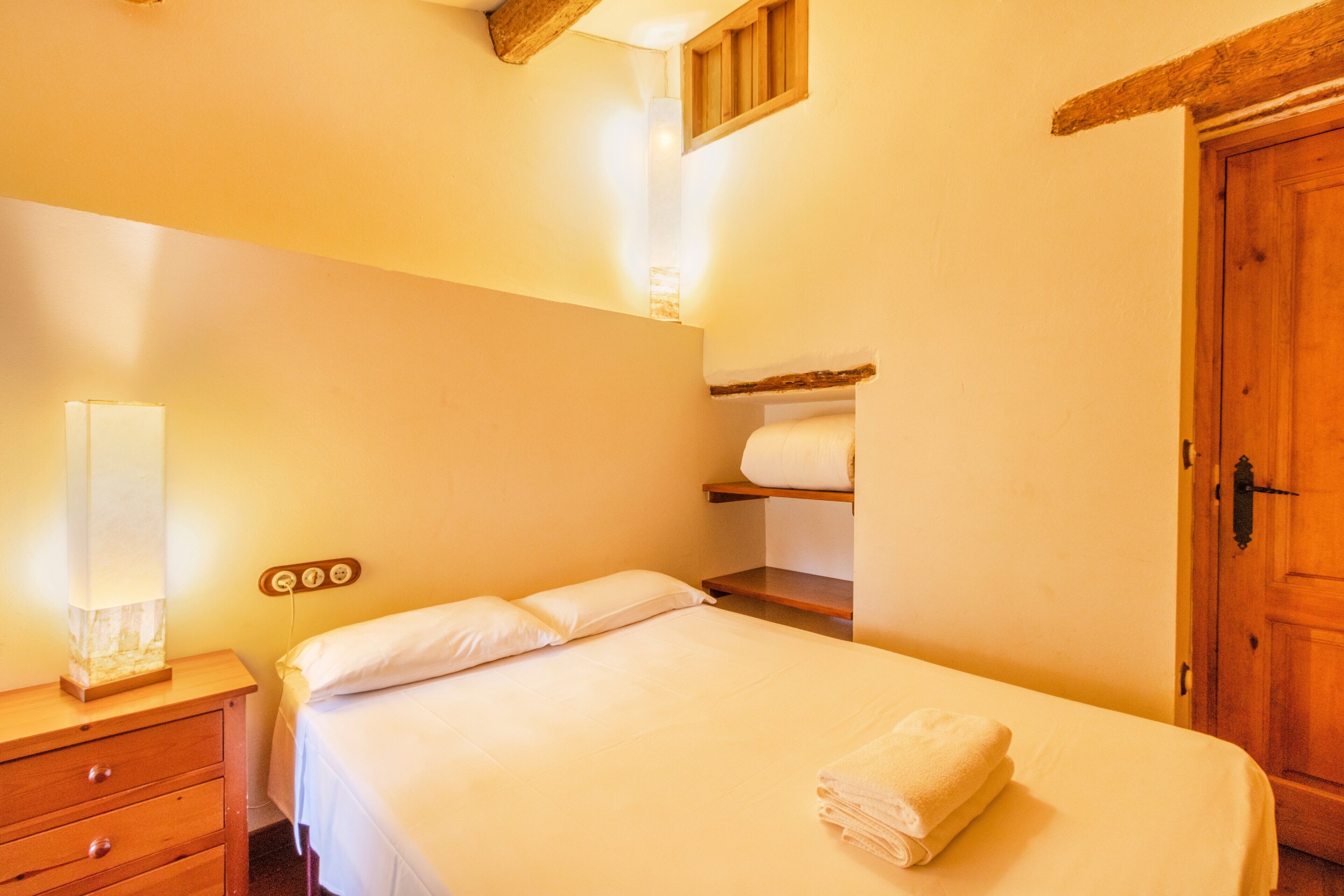 Ein Schlafzimmer mit einem Bett, einem Nachttisch aus Holz, einer Wandleuchte und einer Holztür.