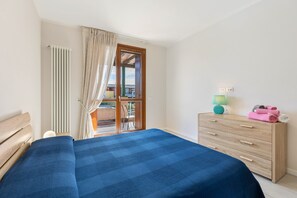Een slaapkamer met een bed, een houten dressoir, een lamp en uitzicht op een balkon.
