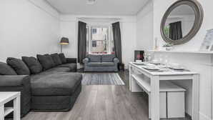 En moderne stue med en grå hjørnesofa, en mindre grå sofa, et hvidt sofabord og et spiseområde med et hvidt bord dækket til fire personer.