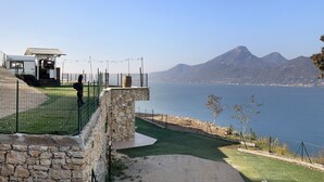 A coastal property with a stone wall, a fenced area, and a view of the sea and mountains. - Mobile Home 'Genziana' with Lake View, Wi-Fi and Air Conditioning (Brenzone)