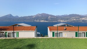 A building with two red-tiled roofs, a fenced area, and a view of mountains and a body of water. - Mobile Home 'Genziana' with Lake View, Wi-Fi and Air Conditioning (Brenzone)