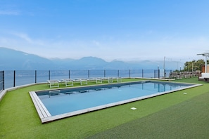 Une piscine rectangulaire dotée d’une terrasse en bois, entourée de gazon synthétique, et offrant une vue sur les montagnes et la mer.