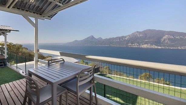 A balcony with a table and chairs, overlooking a body of water and mountains. - Mobile Home 'Genziana' with Lake View, Wi-Fi and Air Conditioning (Brenzone)