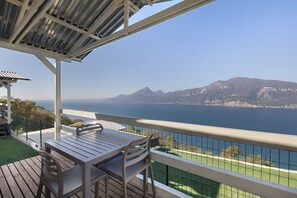 A balcony with a table and chairs, overlooking a body of water and mountains.