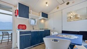 A modern kitchen with blue cabinets, a red fire extinguisher, and a window overlooking a deck. - Mobile Home 'Genziana' with Lake View, Wi-Fi and Air Conditioning (Brenzone)