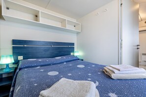 A bedroom with a bed, nightstands, a wall-mounted shelf, and a door.