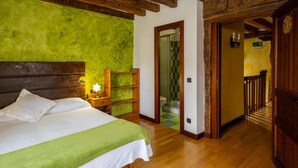 Un dormitorio con cama, cabecero de madera, pared verde y puerta de madera que da al baño.