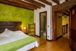 A bedroom with a bed, wooden headboard, green wall, and a wooden door leading to a bathroom.