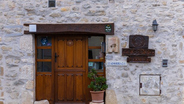 Edificio de piedra con puerta de madera, una planta en maceta y un letrero con un número.