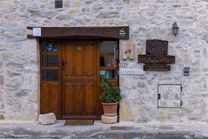 A stone building with a wooden door, a potted plant, and a sign with a number.