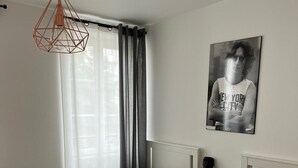 Un dormitorio con dos camas, un candelabro colgante, una ventana con cortinas, un cuadro en la pared y una mesita de noche con una planta.