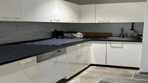 Una cocina compacta con armarios blancos, encimera negra y salpicadero de mármol.