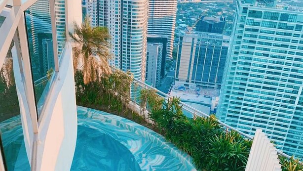 Piscina infinita en la azotea con vista a la ciudad, rodeada de follaje y arquitectura moderna.