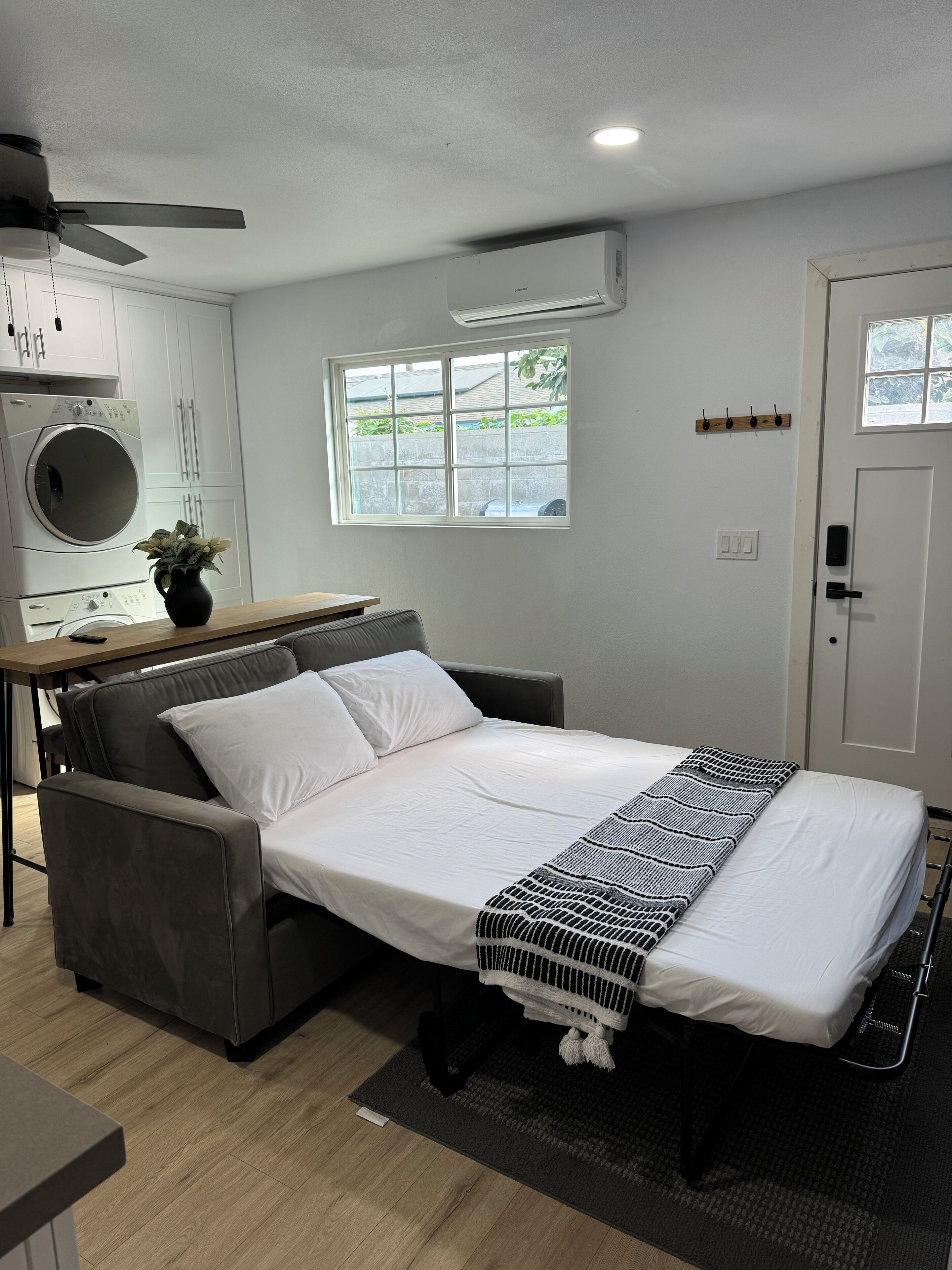 Une chambre moderne équipée d’un lit, d’un bureau, d’une machine à laver et d’une fenêtre.