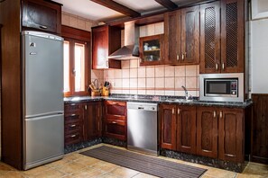 A kitchen with wooden cabinets, a stainless steel refrigerator, a dishwasher, a microwave, and a tiled backsplash. - Country House 'Casa Rural Arroal I' with Mountain View, Wi-Fi and Air Conditioning (Sotoserrano)