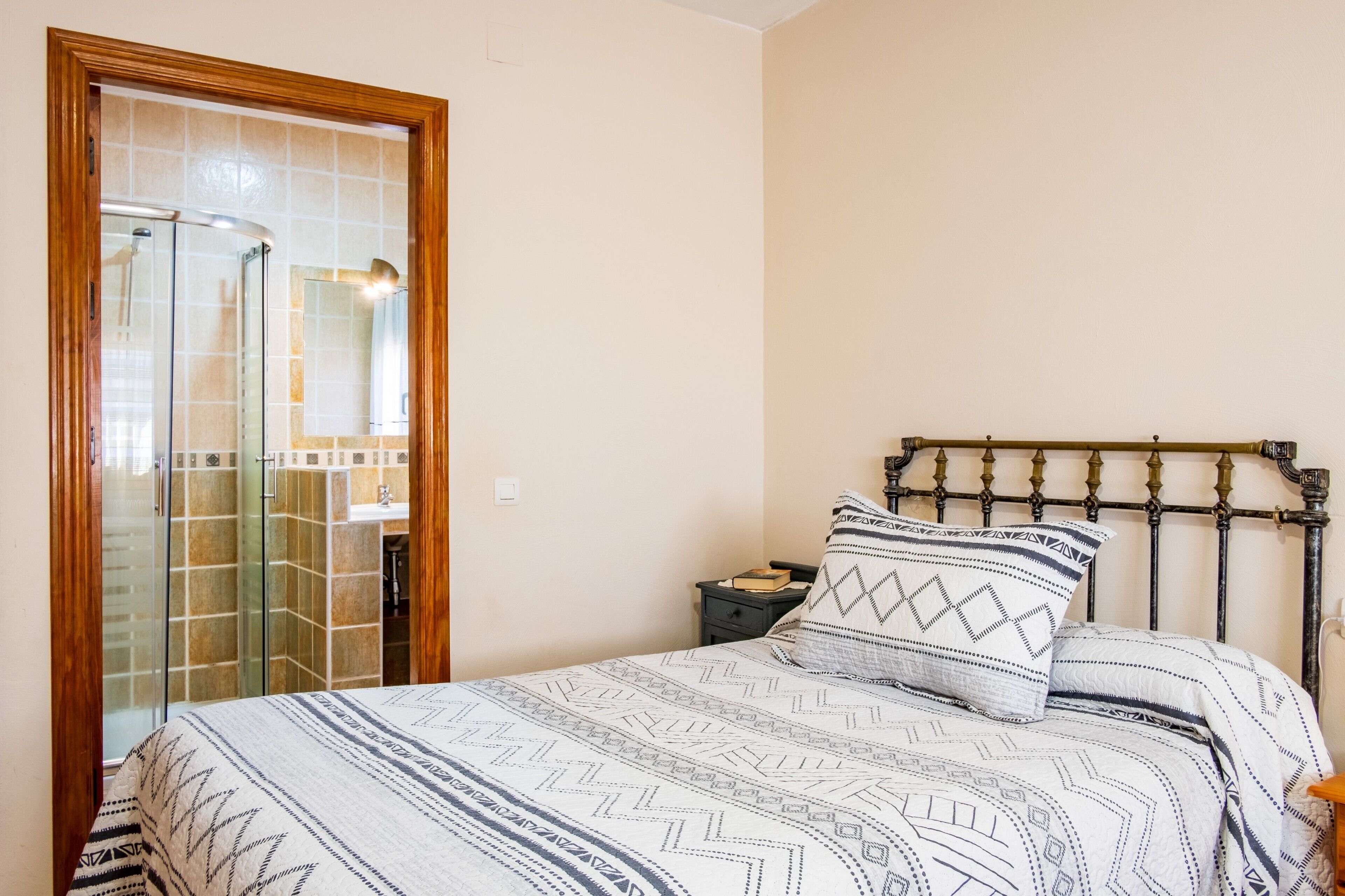 Un dormitorio con cama, mesita de noche, cabecera de madera y mampara de ducha de vidrio.