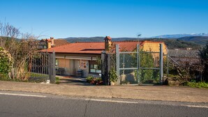Une propriété rurale dotée d’une entrée clôturée, d’un petit bâtiment avec un toit en tuiles et d’un paysage montagneux en arrière-plan.