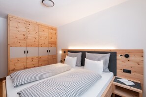 Un dormitorio con cama, dos mesitas de noche, un armario de madera y una lámpara de pared.