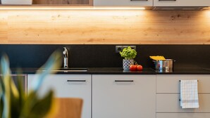 Une cuisine moderne avec des meubles en bois, un plan de travail noir, un évier et un pot de fleurs contenant des plants de tomates.