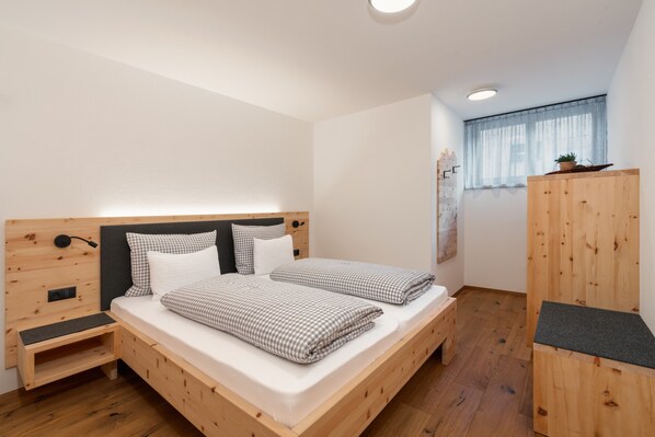 Una habitación con una cama de madera, una mesita de noche pequeña, un armario y una ventana con cortina.