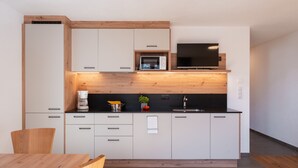 Une cuisine moderne avec des meubles blancs, un plan de travail noir, un four à micro-ondes et un téléviseur.
