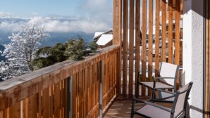 Un balcon en bois offrant une vue sur des arbres couverts de neige et des montagnes lointaines.