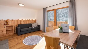 Un espace de vie au sol en bois, comprenant un canapé, une table à manger et offrant une vue sur un paysage enneigé grâce à de grandes fenêtres.