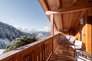 Un balcon en bois offrant une vue sur des montagnes enneigées et des palmiers.