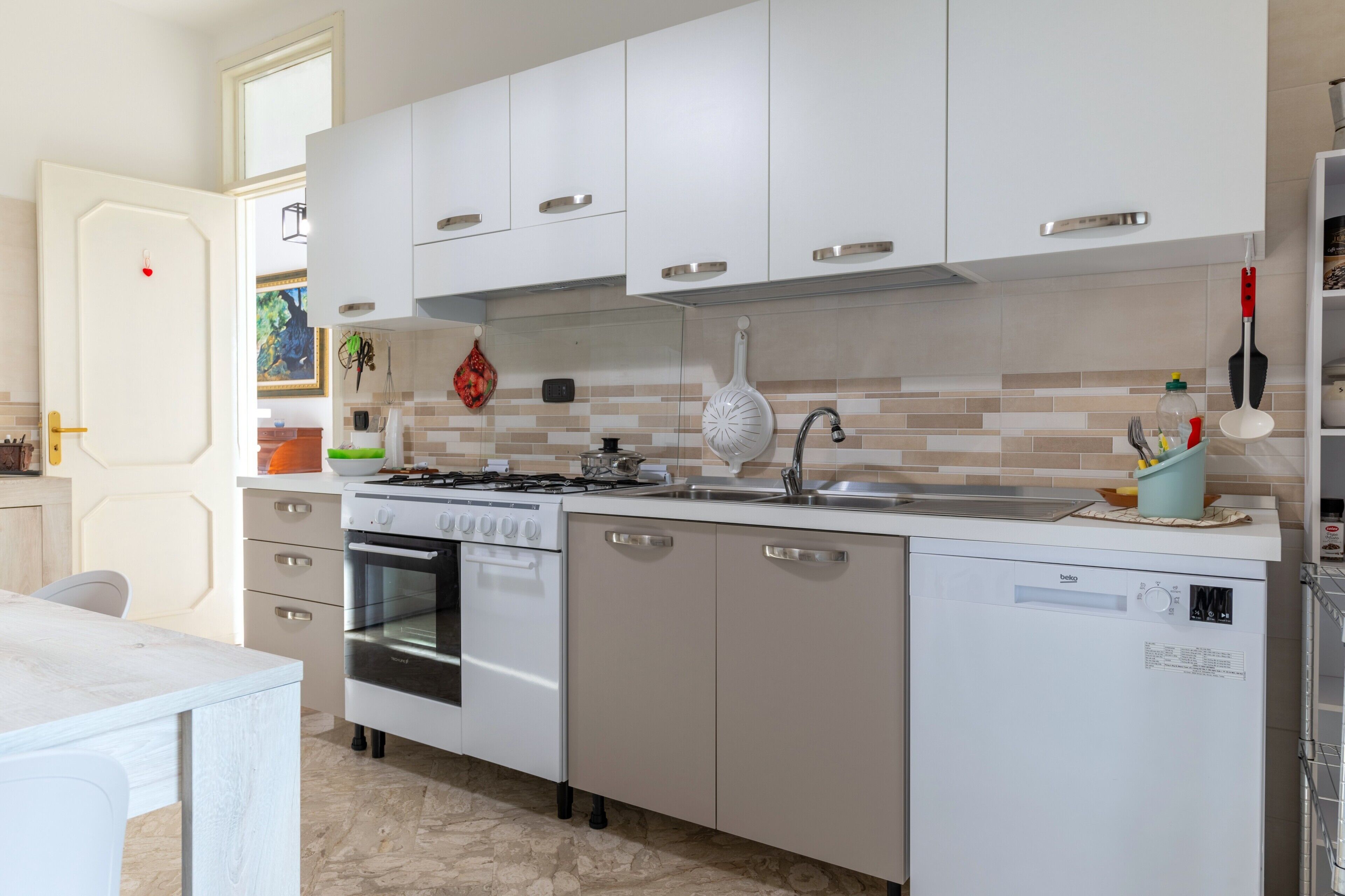 Une cuisine moderne avec des meubles blancs, une cuisinière, un four, un lave-vaisselle et un évier.
