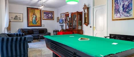 Une table de billard recouverte d’un drap vert, un canapé, un téléviseur et des œuvres d’art encadrées accrochées aux murs.
