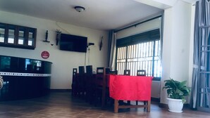 Un coin repas avec une nappe rouge, des chaises en bois, un téléviseur fixé au mur et une plante en pot.