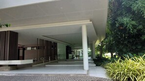 A modern building entrance with a covered walkway, a brick-paved area, and greenery.