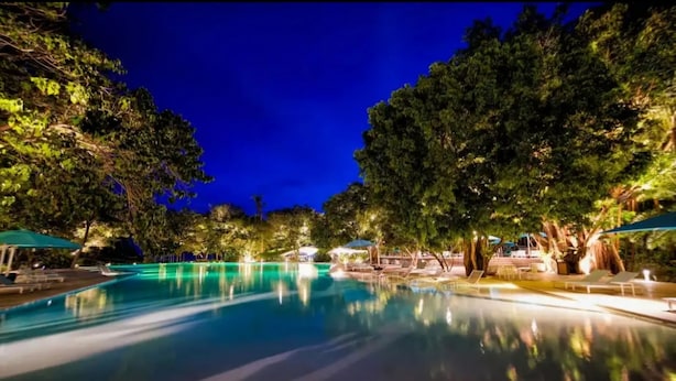 A nighttime swimming pool with lounge chairs and umbrellas, surrounded by trees.