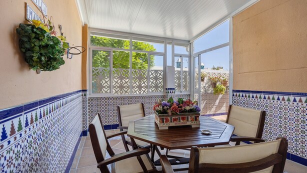 Un patio cubierto con un muro de azulejos, una mesa con sillas y una planta decorativa.