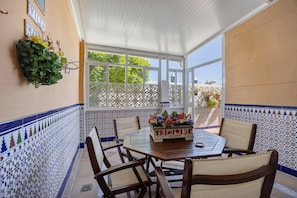 Un patio couvert avec un mur recouvert de carreaux, une table avec des chaises et une plante décorative.