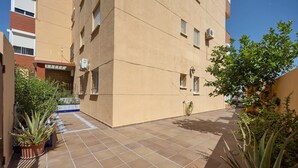 Un patio con suelo de baldosas, plantas en macetas y un edificio con varias ventanas y unidades de aire acondicionado.