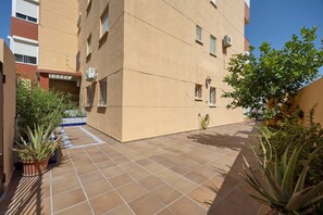 Une cour avec un sol carrelé, des plantes en pot et un bâtiment doté de nombreuses fenêtres et de climatiseurs.
