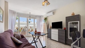 Una sala de estar moderna con un sofá, una mesa de centro de vidrio, un televisor y un comedor con sillas y una mesa.