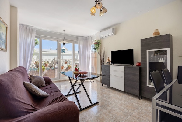 Un salon moderne comprenant un canapé, une table basse avec un plateau en verre, un téléviseur et un coin repas avec des chaises et une table.