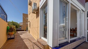 Un edificio residencial con un patio empedrado, una puerta corrediza de vidrio y un pequeño espacio exterior con asientos.