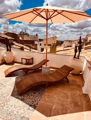 Terraço no topo com cadeiras de descanso, um guarda-sol grande e um vaso decorativo.