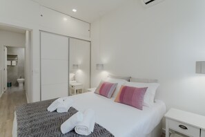Ein modernes Hotelzimmer mit Bett, Nachttisch, Kleiderschrank und einem Badezimmer im Hintergrund.