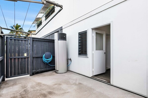 A clean, modern outdoor area with a concrete floor, a metal air conditioning unit, a wooden gate, and a blue hose coiled on the ground.