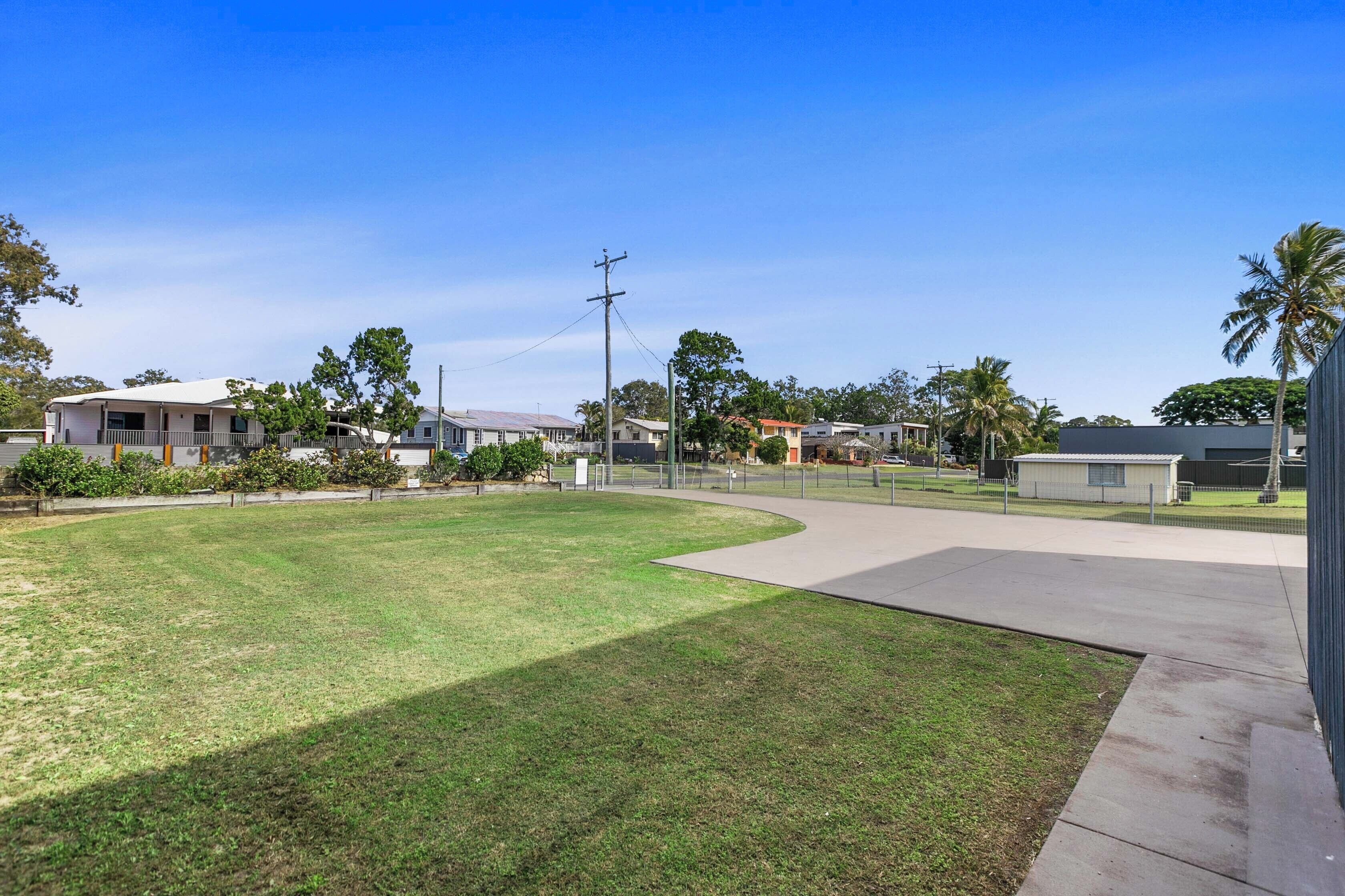 A residential area with a grassy lawn, a curved driveway, and houses in the background.