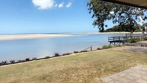 Blick auf einen Strand mit einer Rasenfläche, einer Holzterrasse und einem Metallgeländer.