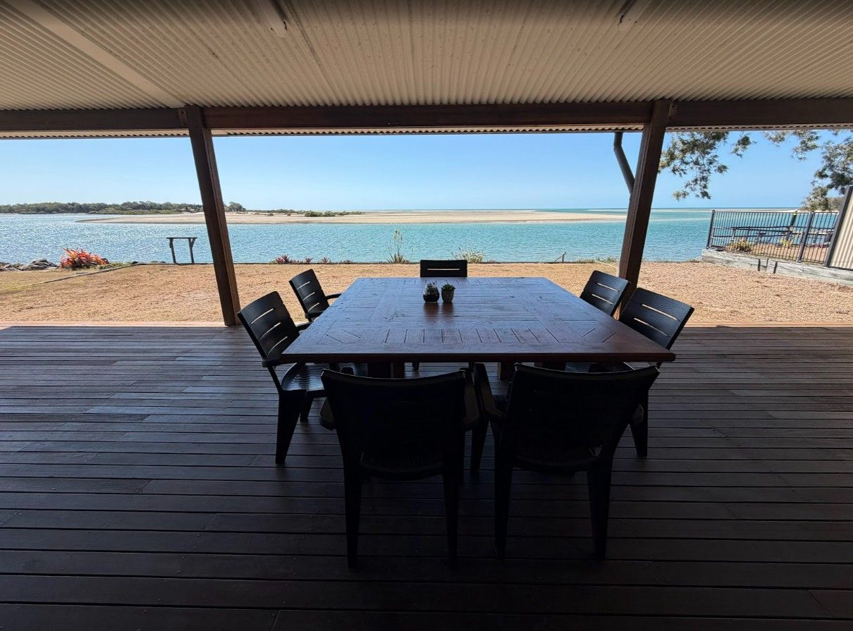 A covered outdoor dining area with a table and chairs, overlooking a beach and water.
