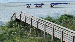 Een strand met houten looppaden die leiden naar strandstoelen en parasols.